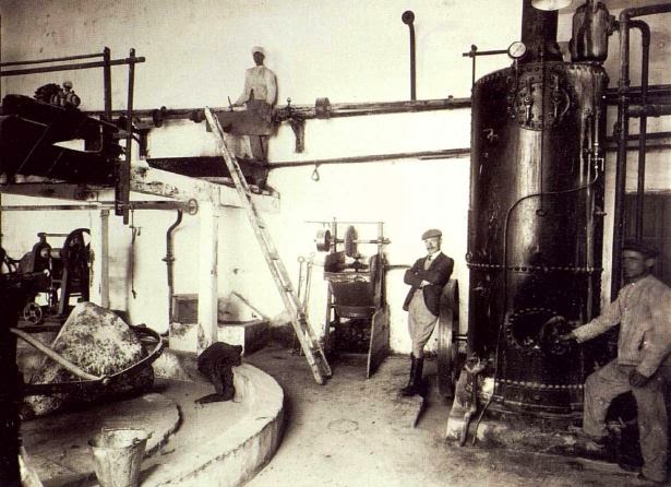 Fotografía histórica del interior de un molino de aceite con operarios y maquinaria.
