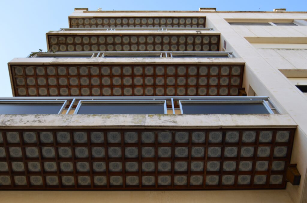 Fachada de edificio con balcones y filas de pequeñas ventanas vistas desde abajo.