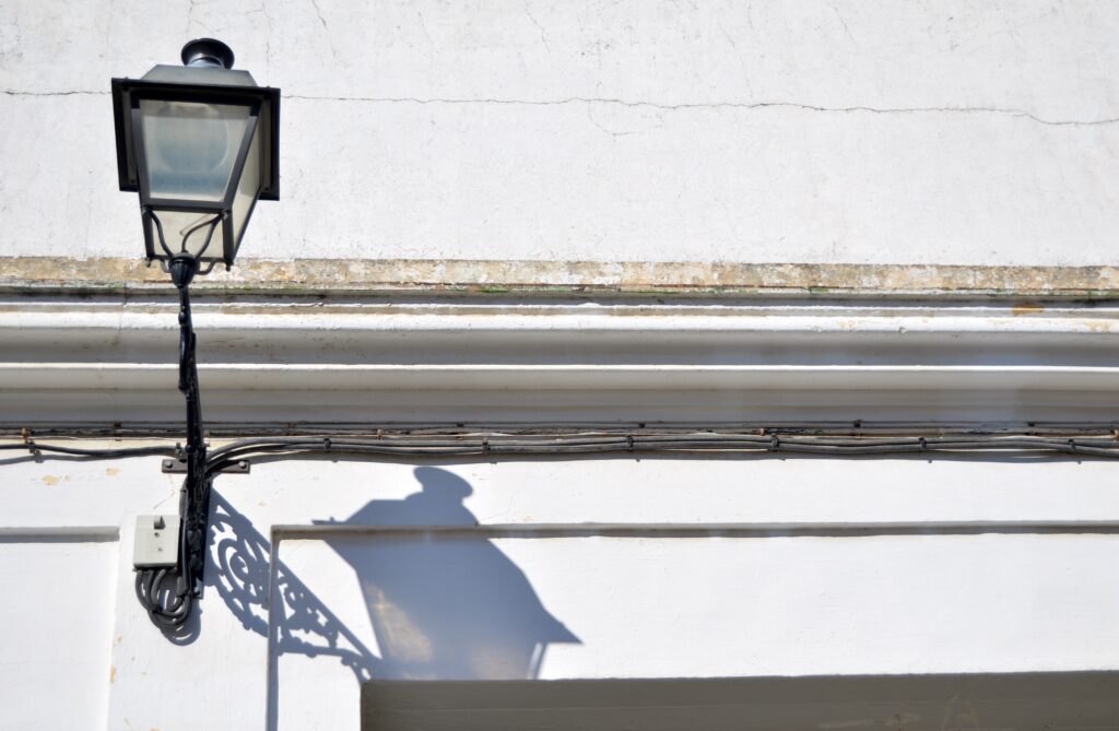 Farola y sombra proyectada sobre un muro blanco.