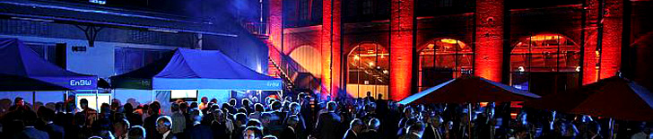 Sala interior iluminada en rojo y azul con público sentado.
