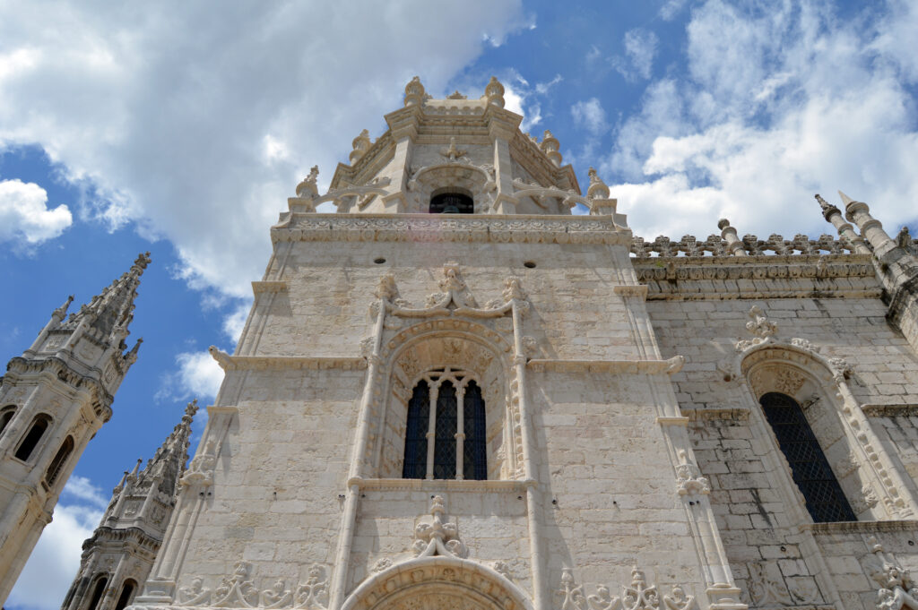 Fachada de piedra con ventanas y frontón bajo un cielo con nubes.