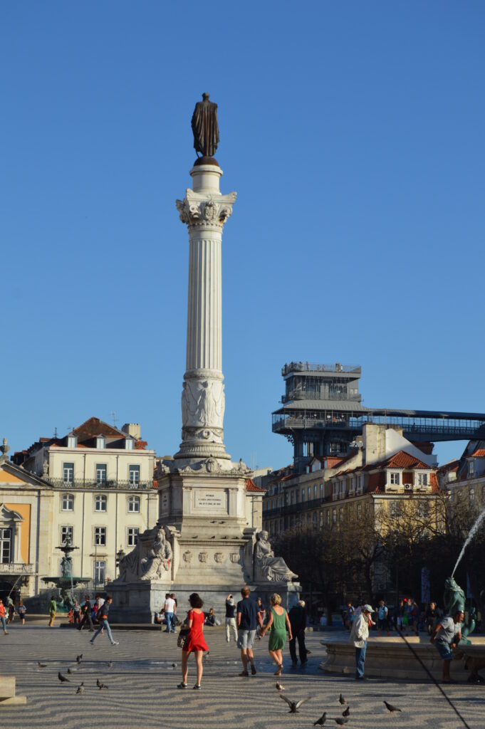 Plaza pavimentada con una columna alta y edificios históricos al fondo.